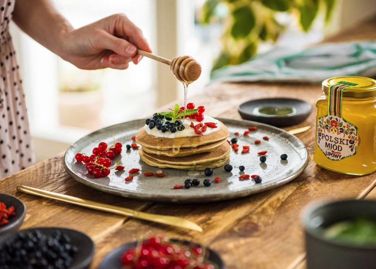 Ręka lejąca miód z czerpaka na naleśniki z owocami - zdjęcie jedzenia wykonane w Olsztynie