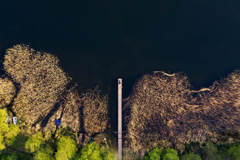 Narzeczeni leżący na pomoście nad jeziorem Kortowskim fotografia ślubna z drona sesja narzeczeńska