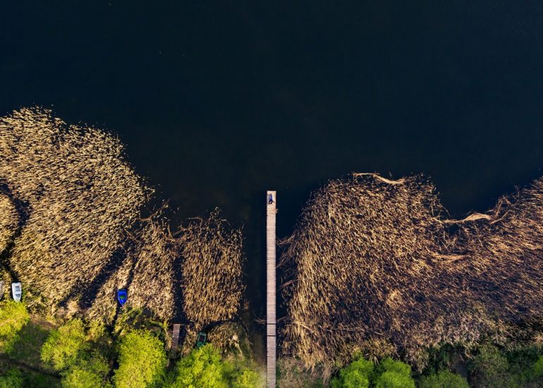 Narzeczeni leżący na pomoście nad jeziorem Kortowskim fotografia ślubna z drona sesja narzeczeńska