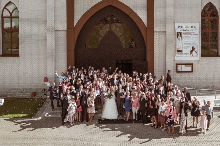 Zdjęcie grupowe ze ślubu pod kościołem fotografia z drona w województwie warmińsko-mazurskim