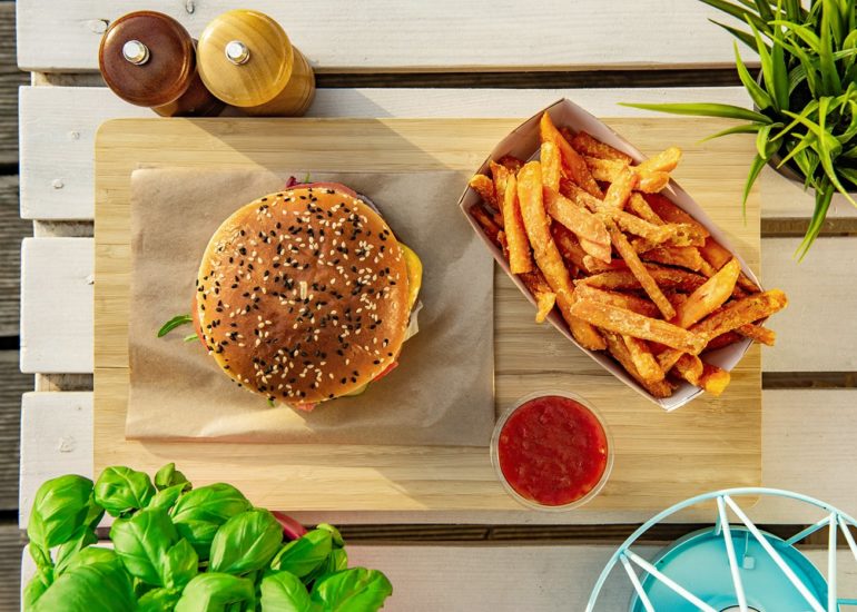 Widok z góry na burgera z frytkami i sosem na tle białego stołu z palet