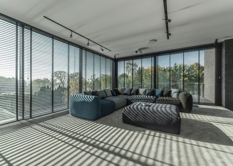 Kanapa oświetlona słońcem wpadającym do pomieszczenia przez uchylone rolety okienne