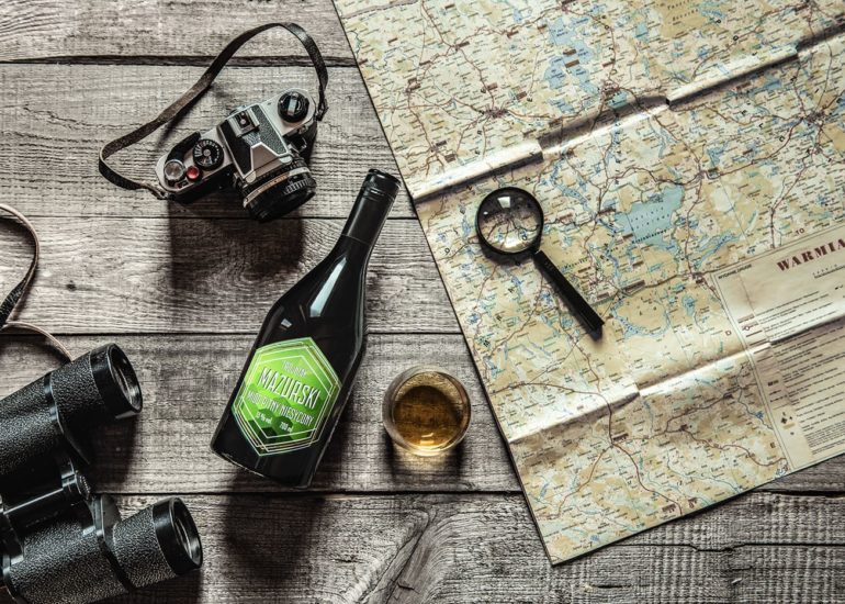 Miód pitny Mazurski - widok z góry na butelkę, lornetkę, aparat i starą mapę Warmii i Mazur flatlay