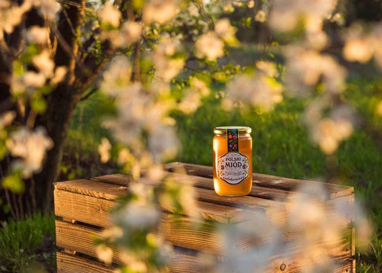 Słoik miodu w wiosennej scenerii z kwitnącymi kwiatami w trakcie zachodu słońca - fotografia reklamowa