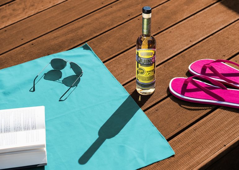 Butelka pigwówki na pomoście latem w otoczeniu przyborów plażowych