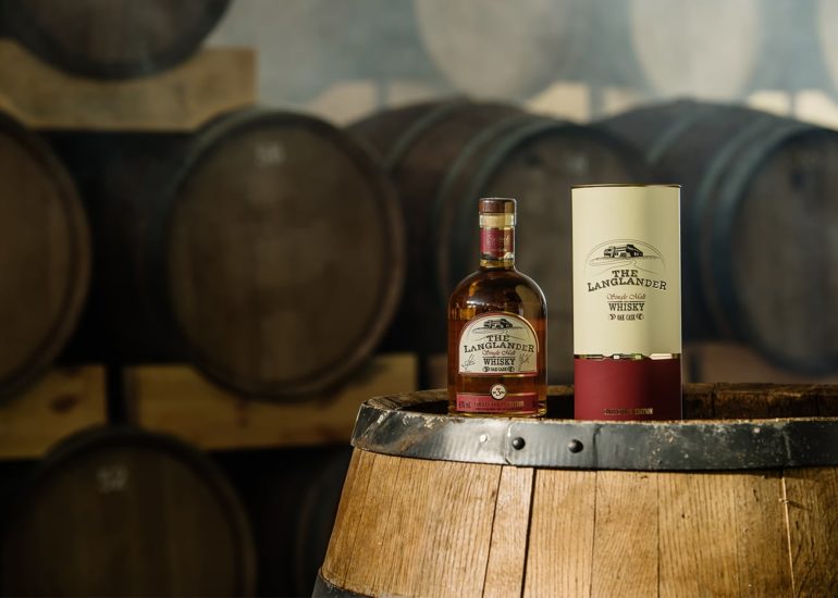 Butelka polskiej whisky Langlander z opakowaniem prezentowym na tle dębowych beczek - fotografia reklamowa Olsztyn