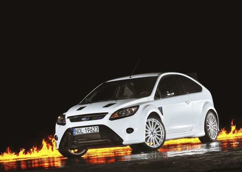 Ford Focus RS na tle płomieni ognia odbijających się w mokrym podłożu - fotografia motoryzacyjna