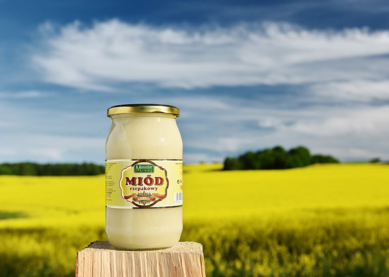 Miód rzepakowy na tle dużego pola rzepaku w trakcie kwitnięcia