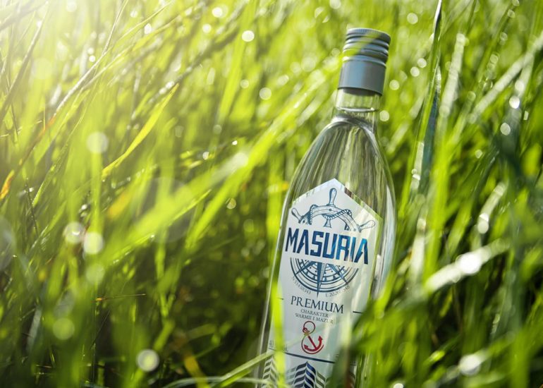 Butelka wódki Masuria w trawie z rosą o poranku fotograf reklamowy Olsztyn