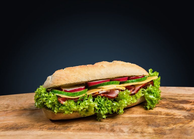 Apetyczny sandwich z szynką, serem żółtym, ogórkiem zielonym, rzodkiewką i sałatą na ciemnogranatowym tle - fotografia kulinarna