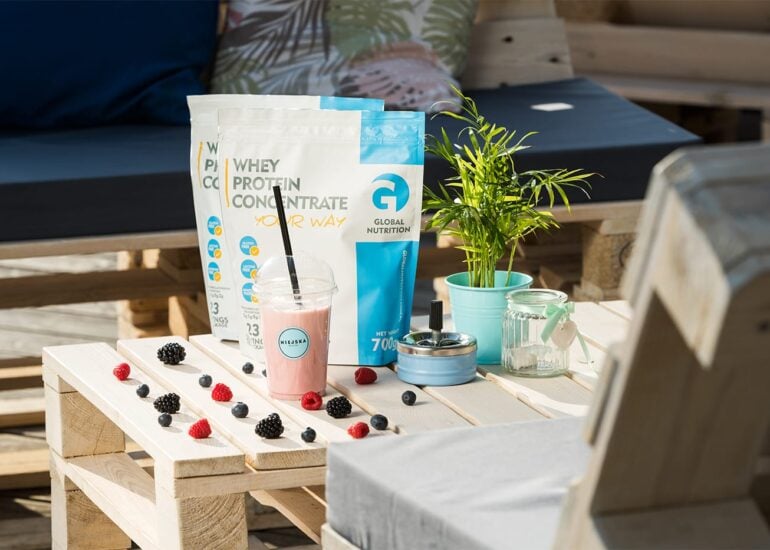 Shake mleczny proteinowy z opakowaniem odżywki białkowej i owocami rozrzuconymi na stole z palet drewnianych