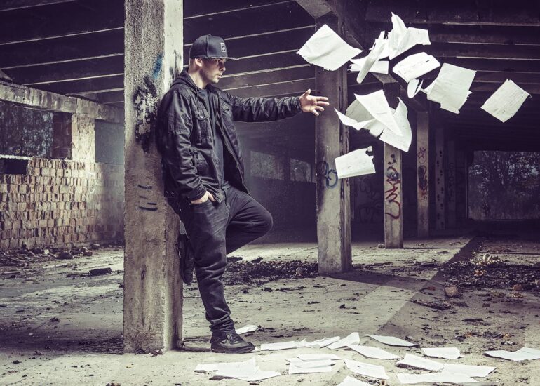 Raper Mejdż rozrzucający kartki notesu w industrialnym garażu - zdjęcie na okładkę płyty CD